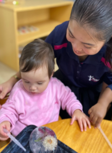 A teacher working one-on-one with a child at an ice melting activity table indoors.