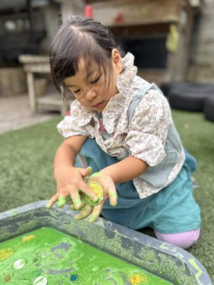 A child exploring green messy play with their hands at a sensory table.