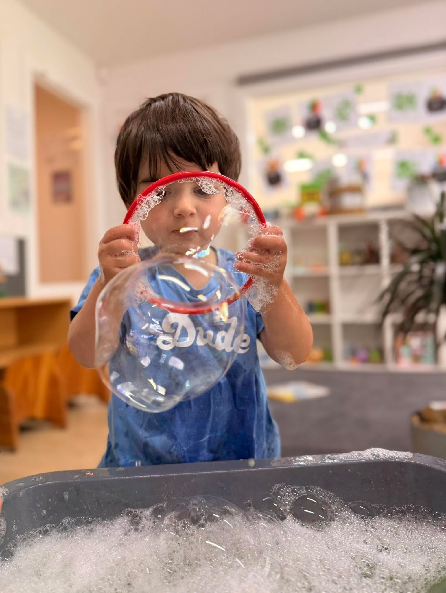 A child closely examining bubbles at sensory play table.