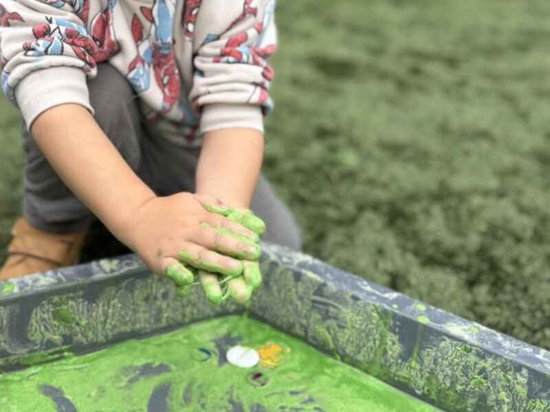A toddler playing with sensory gloop in an activity table outdoors