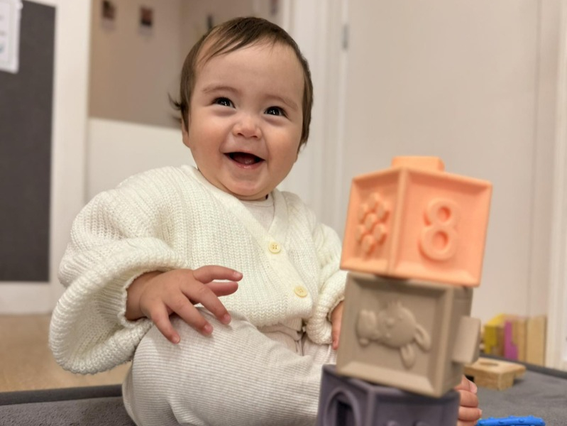 A smiling baby playing with blocks on a mat on the floor
