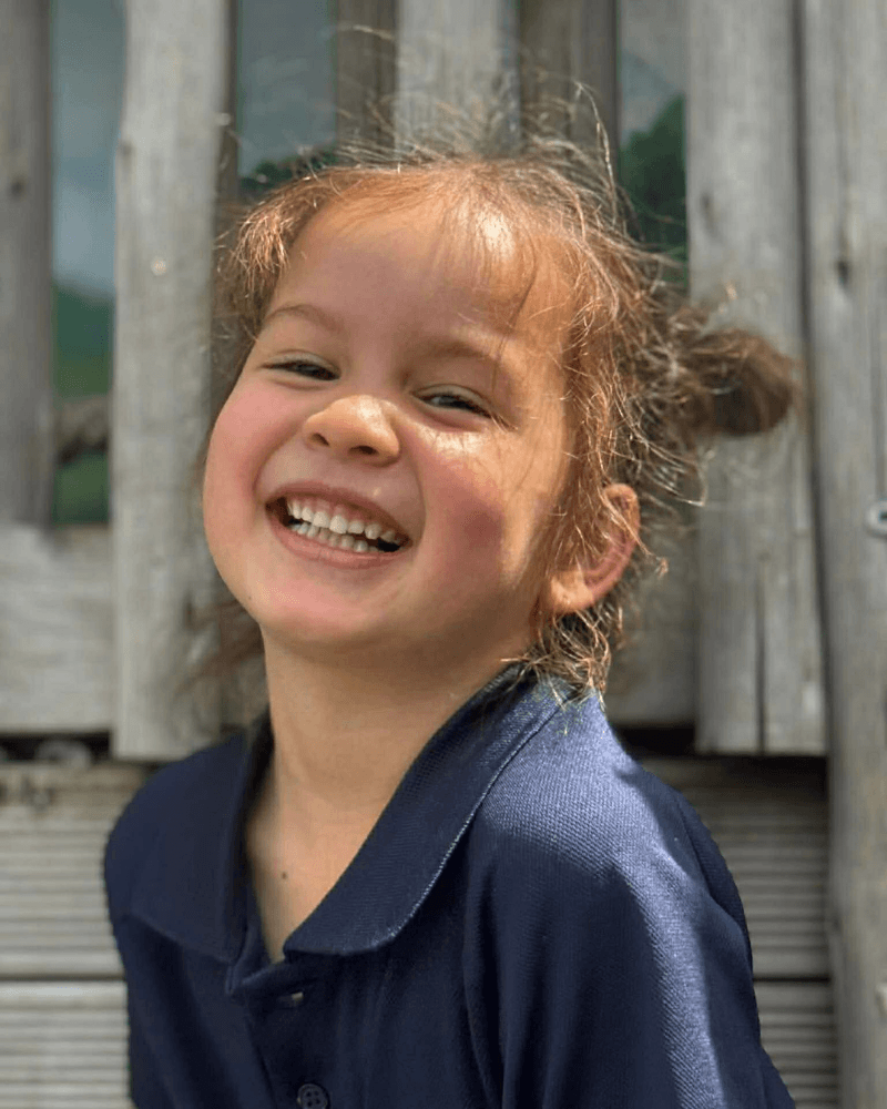 A happy young girl smiling outdoors at KidsCo Birkenhead childcare centre.