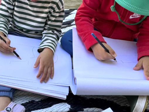 Two pre-school children writing on paper with pencils outdoors
